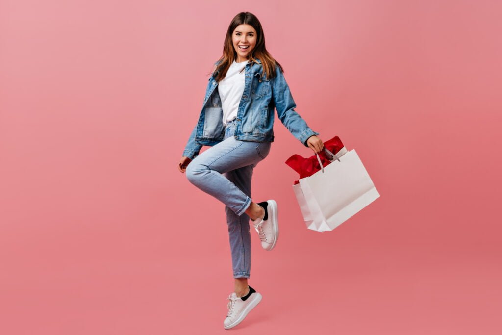 pleased young woman holding store bag full length view of charming european girl in denim attire