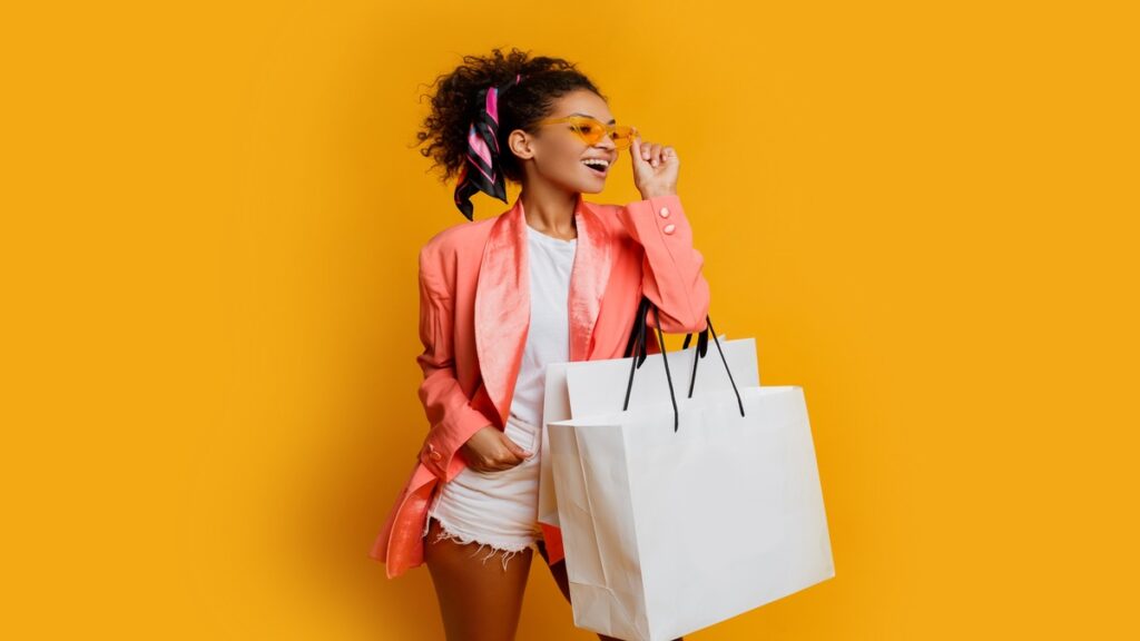 studio shot of pretty black woman with white shopping bag standing over yellow background trendy spring fashionable look
